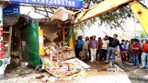 An unauthorized structure raised on footpath near Rail Head Complex Jammu, being demolished by JMC on Friday.