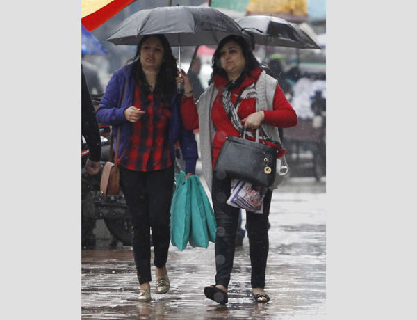 Women tourists hold umbrella while walking on a footpath at Residency Road in Srinagar on Friday. — Excelsior Photo