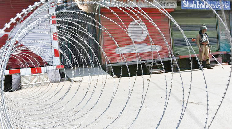 An Indian policeman stands guard next to concertina wire laid across a road during a curfew in Srinagar