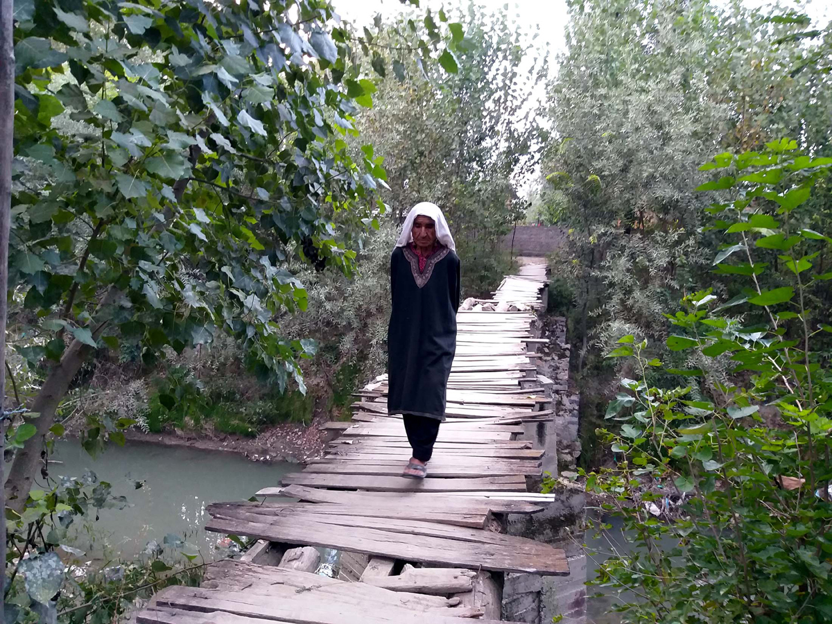 An elderly woman walks over a makeshift bridge at Warbagh in Pulwama. — Excelsior/Younis Khaliq