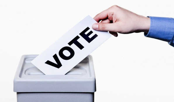 A man putting a ballot with the word VOTE written on it into a ballot box, close-up hands