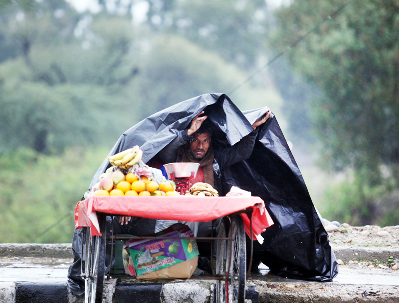 A wayside fruit seller takes a cover of polythene sheet to protect himself from heavy rain in Jammu on Tuesday. -Excelsior/Rakesh A wayside fruit seller takes a cover of polythene sheet to protect himself from heavy rain in Jammu on Tuesday. -Excelsior/Rakesh