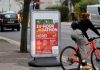 A cyclist rides a bike past a sign for a 24-hour vaccination centre, in London
