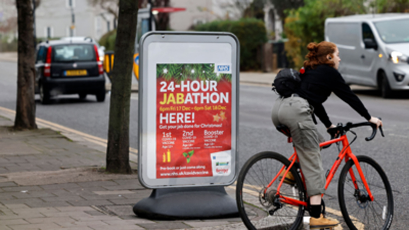 A cyclist rides a bike past a sign for a 24-hour vaccination centre, in London A cyclist rides a bike past a sign for a 24-hour vaccination centre, in London