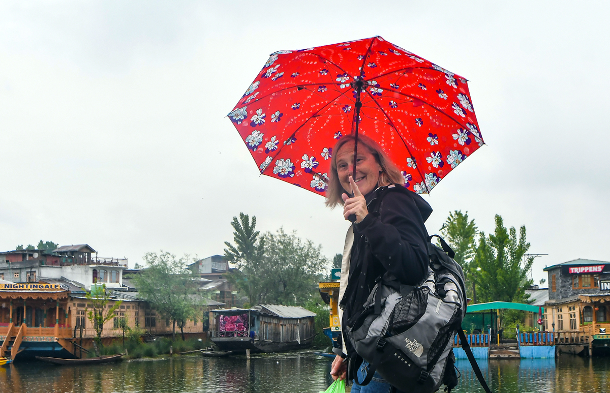 A foreigner tourist takes cover of umbrella during a rain in Srinagar on Tuesday. — Excelsior/Shakeel A foreigner tourist takes cover of umbrella during a rain in Srinagar on Tuesday. — Excelsior/Shakeel