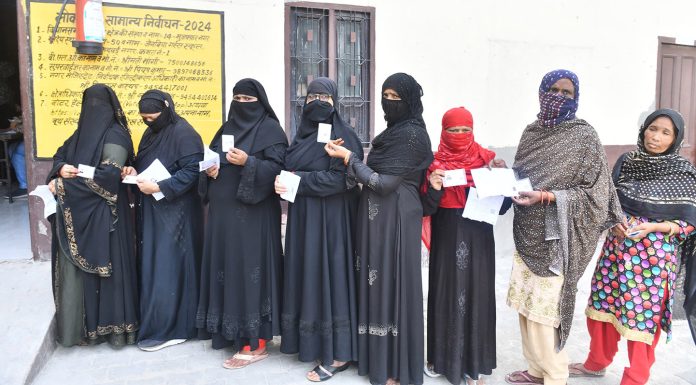 Women show their voters identity cards while waiting in a queue to cast their at a polling station, in Muzafarnagar, Uttar Pradesh on Friday. (UNI)