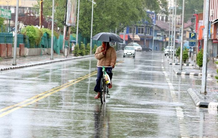 A cyclist takes umbrella cover amid heavy rains in Srinagar on Monday. Excelsior/Shakeel