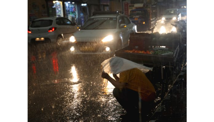 A vegetable vendor takes shelter from rain under a plastic sheet in Jammu. Another pic on page 4. -Excelsior/Rakesh