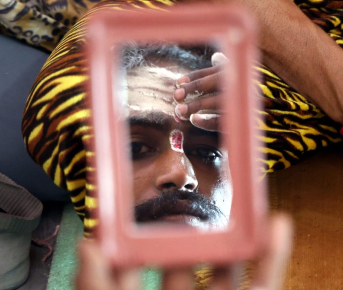 A Sadhu applies ‘Tilak’ on his forehead as he waits to get registered for the annual Amarnath yatra in Jammu. -Excelsior/Rakesh