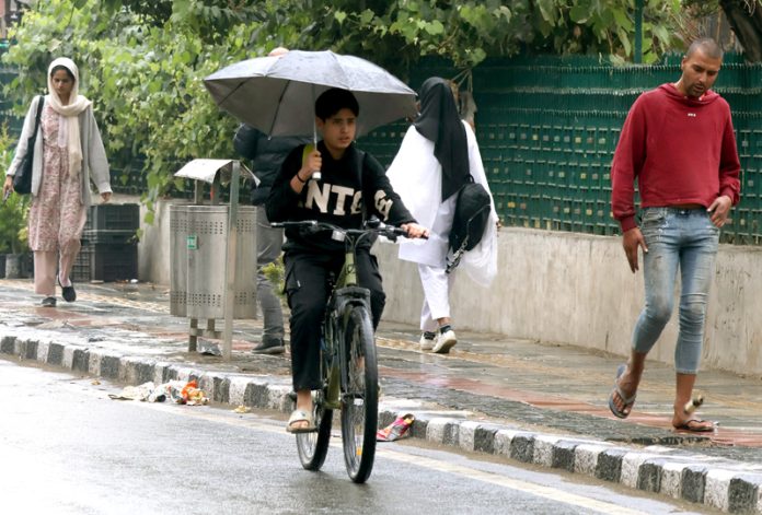 People walking with umbrellas as Srinagar gets a brief rains hower, while snowfall blankets the upper reaches on Tuesday. -Excelsior/Shakeel