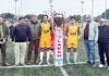 Dignitaries pose with the captains of the two teams alongside the LAKSH Trophy during the inaugural match at Parade Ground, Jammu, on Tuesday.