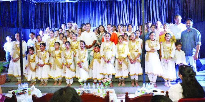Children in cultural dresses posing during a programme alongside dignitaries.