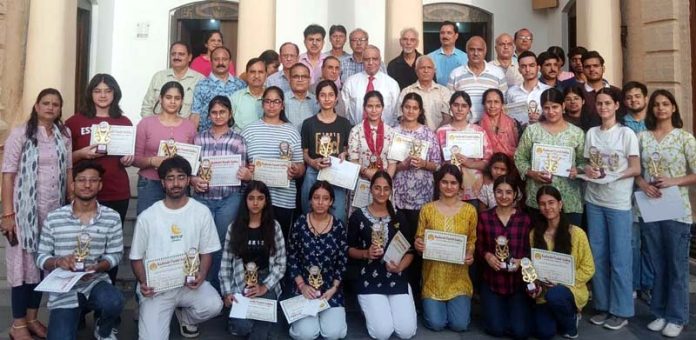 Meritorious students posing along with certificates alongside dignitaries.
