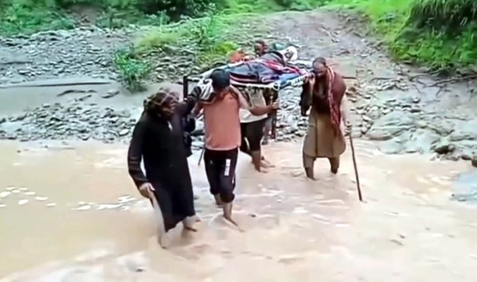 Villagers carrying a patient to hospital on a cot in the absence of a bridge and road to Nowshera village. -Excelsior/Imran