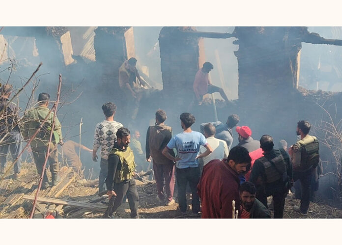 People stand near a burnt house in Ramban district on Friday. -Excelsior/Parvez Mir People stand near a burnt house in Ramban district on Friday. -Excelsior/Parvez Mir