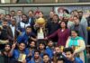 Winning team posing along with trophy and dignitaries.