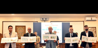 LG Manoj Sinha, along with dignitaries, posing with the Special Cover (postal envelope) released to commemorate J&K’s Ranji Trophy victory during a programme at Lok Bhawan.