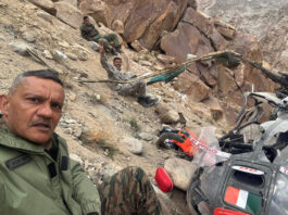 Senior Army officer takes selfie with damaged helicopter and injured officers in background.