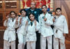 Caption: Judo athletes posing for a group photograph with their coach.
