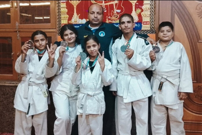 Caption: Judo athletes posing for a group photograph with their coach. Caption: Judo athletes posing for a group photograph with their coach.