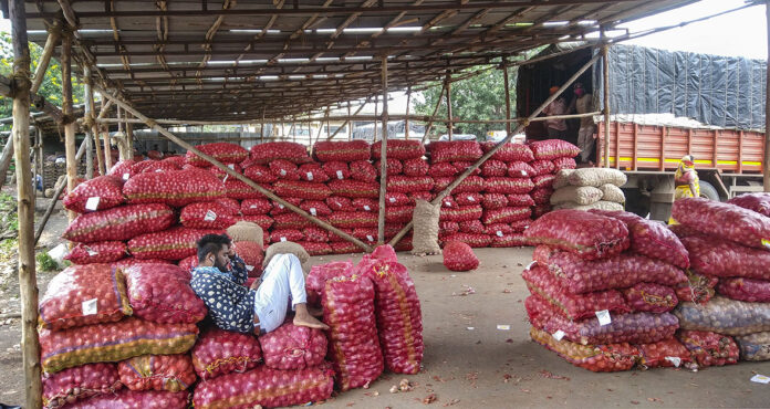 FILE - A worker rests on onions at a market. Agriculture. Farmer, vegetable market